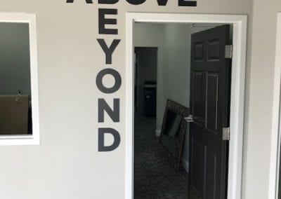PVC cut letters adhered to the wall at the edge of a door frame ABOVE BEYOND